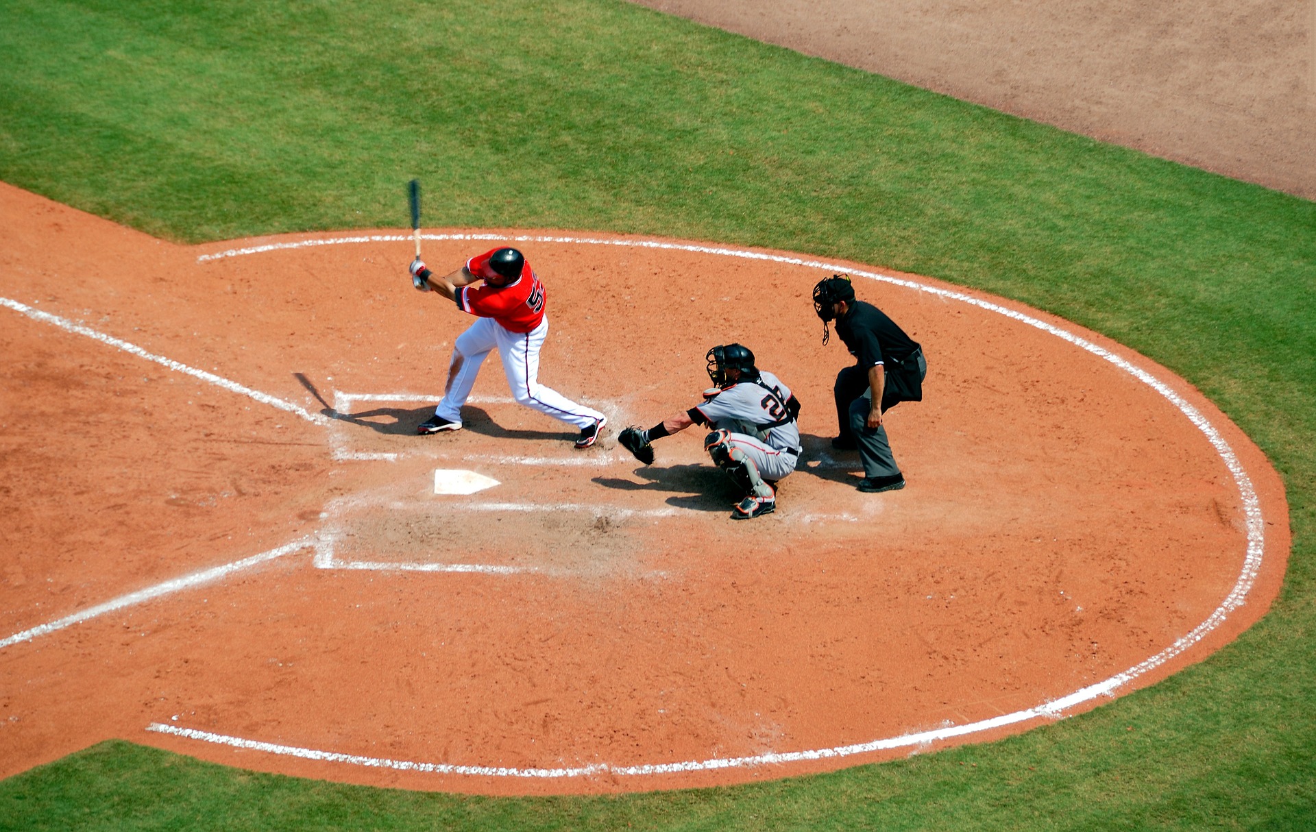 Baseball batter hitting a ball while the catcher stands behinds him: Baseball vs Softball [MindfuseBaseball.com]