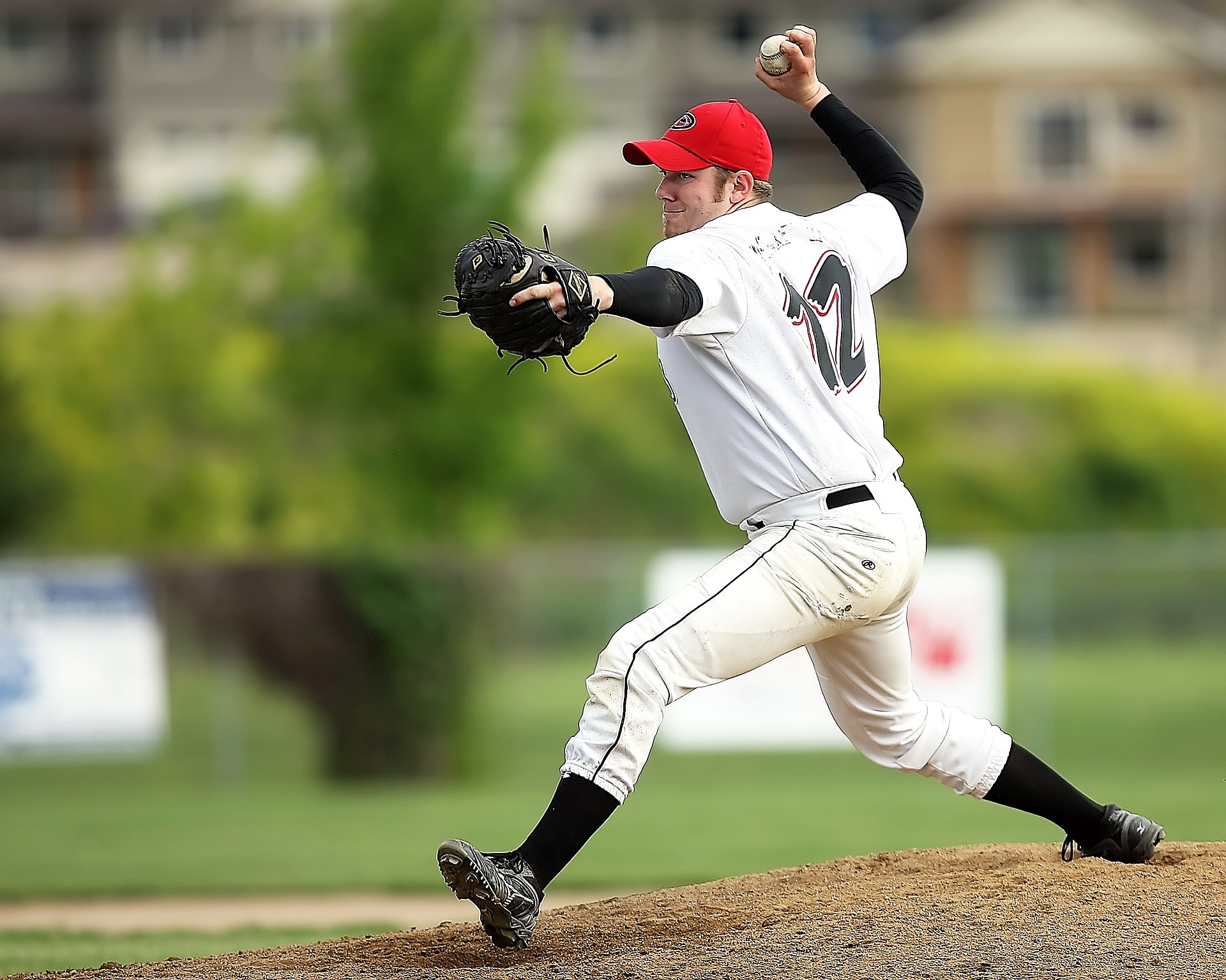 Baseball pitcher in white clothes and red hat just about to pitch a ball to the batter: Types of Baseball Gloves [Mindfusebaseball.com]